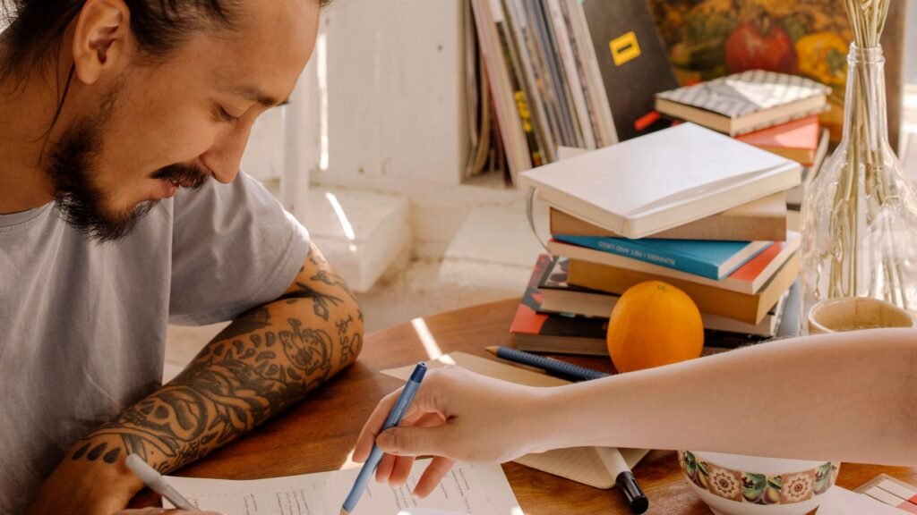 Estudante escrevendo enquanto outra pessoa aponta para suas anotações